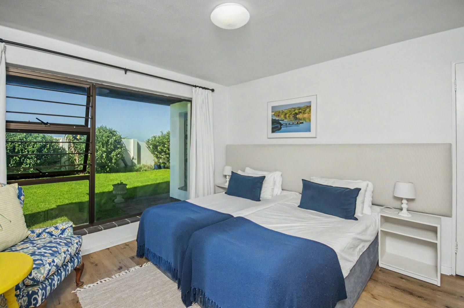Bedroom with navy bedding made up as two single beds, with a large window onto the garden